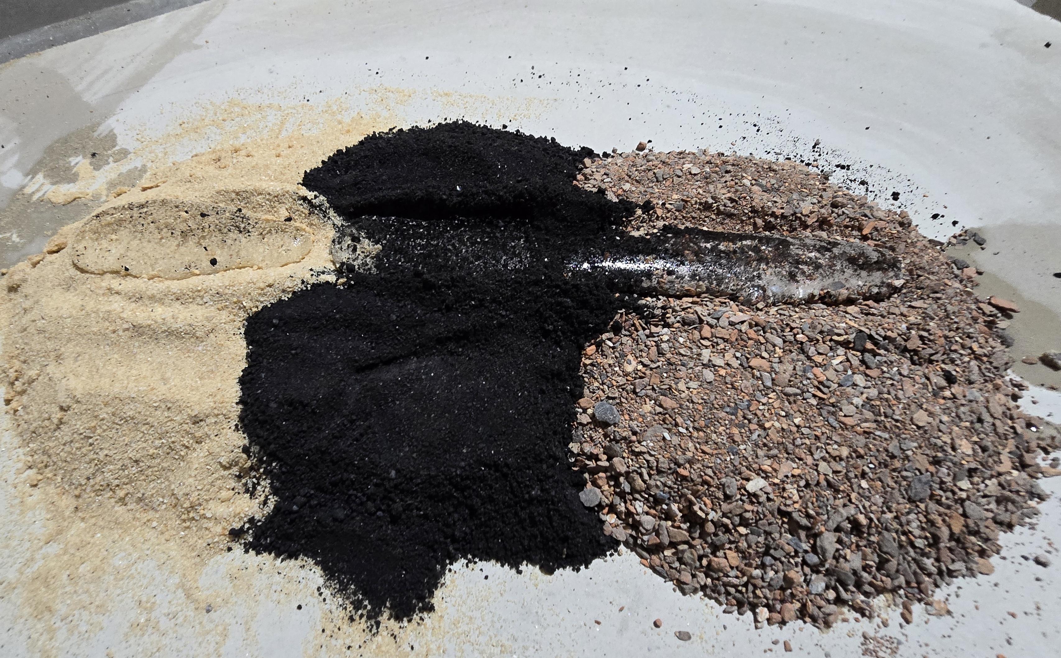 Three piles left to right: normal sand, Big Cajun bottom ash, and Gilberton bottom ash, with a water bead trail across the tops.